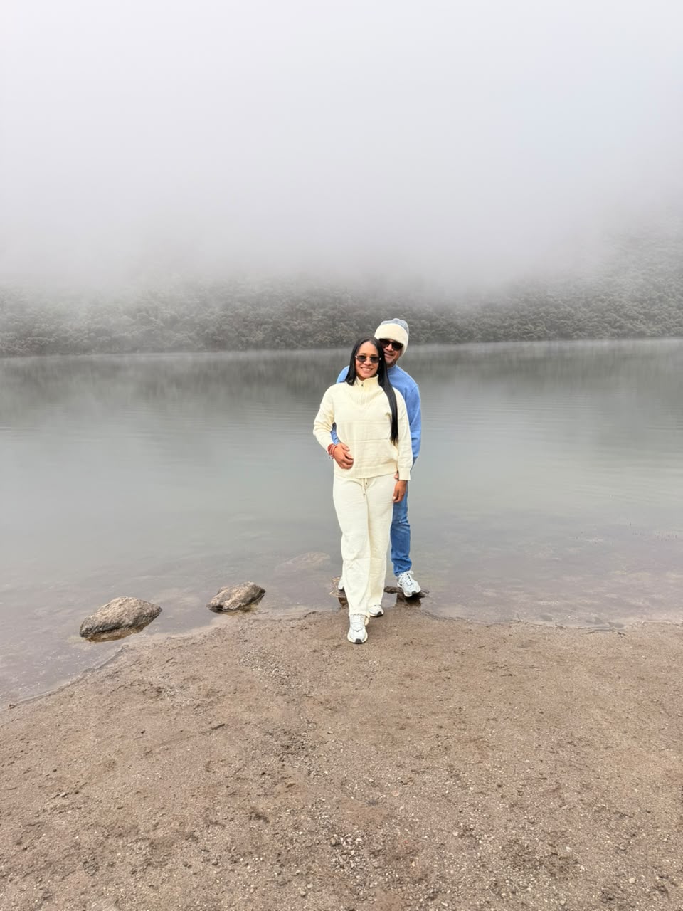 Wilmer y Leydi abrazados frente a un lago entre montañas y neblina.